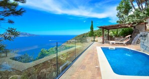 Una piscina privada con barandilla de vidrio y vista al mar.