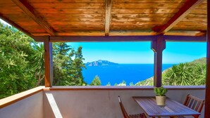 Een overdekt balkon met een tafel en stoelen, met uitzicht op de kust, bergen en zee.