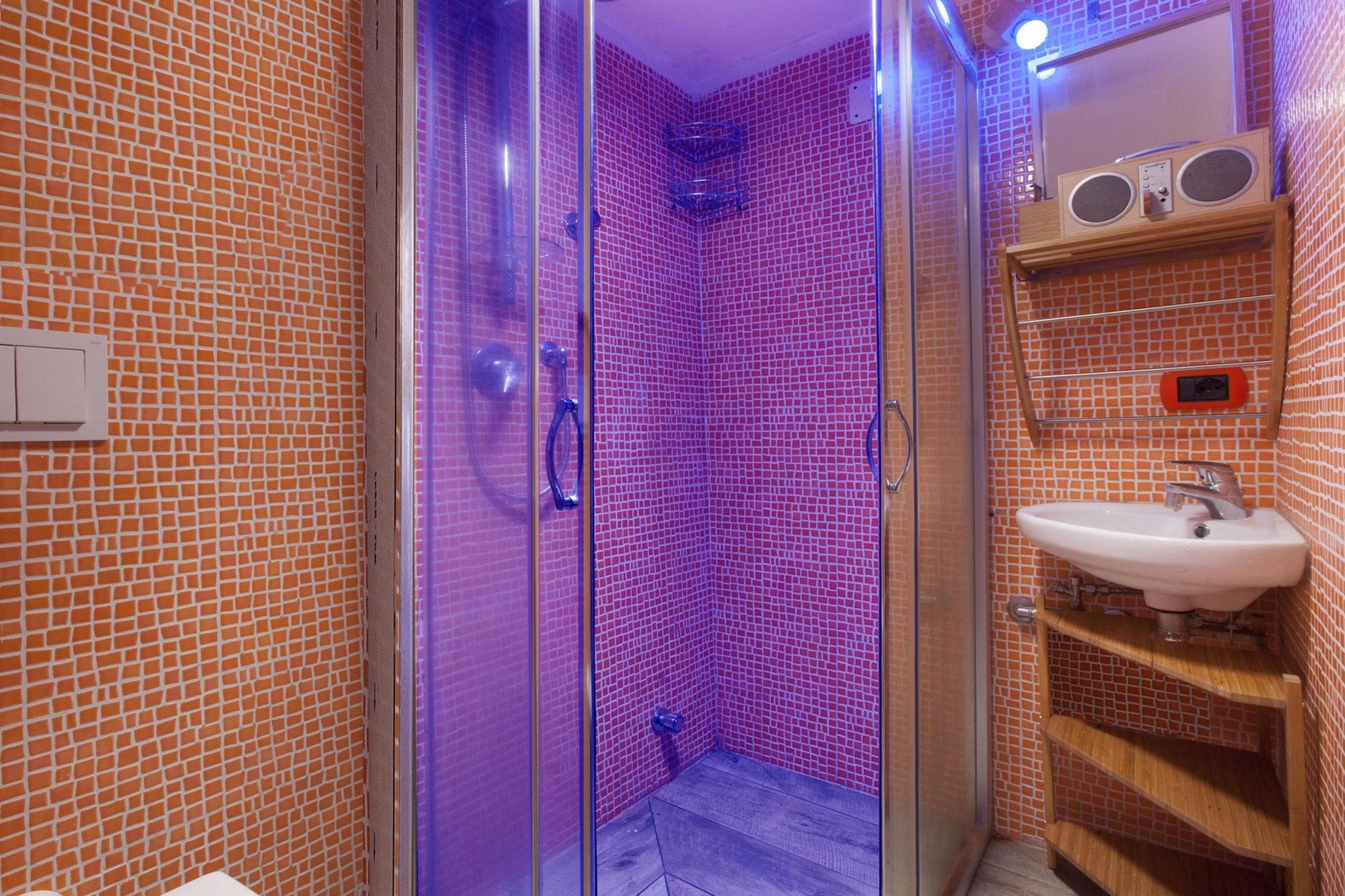 Un bagno con cabina doccia in vetro, un lavandino con una radio sopra e una parete rivestita in piastrelle.