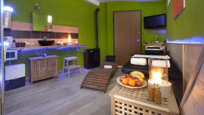 Um espaço de estar compacto com cozinha compacta, uma TV na parede, um banco de madeira, uma mesa com frutas e uma sauna.