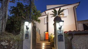Escadaria que leva a uma villa, com uma parede de pedra de um lado e uma árvore do outro.