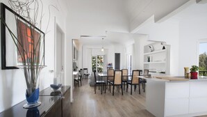 Et moderne køkken med hvide skabe, en central ø og et spiseområde med stole og borde.