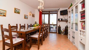 A dining area with a wooden table and chairs, a television mounted on the wall, and a bookshelf filled with books. - Casa Tatano in Massa Lubrense (Massa Lubrense)