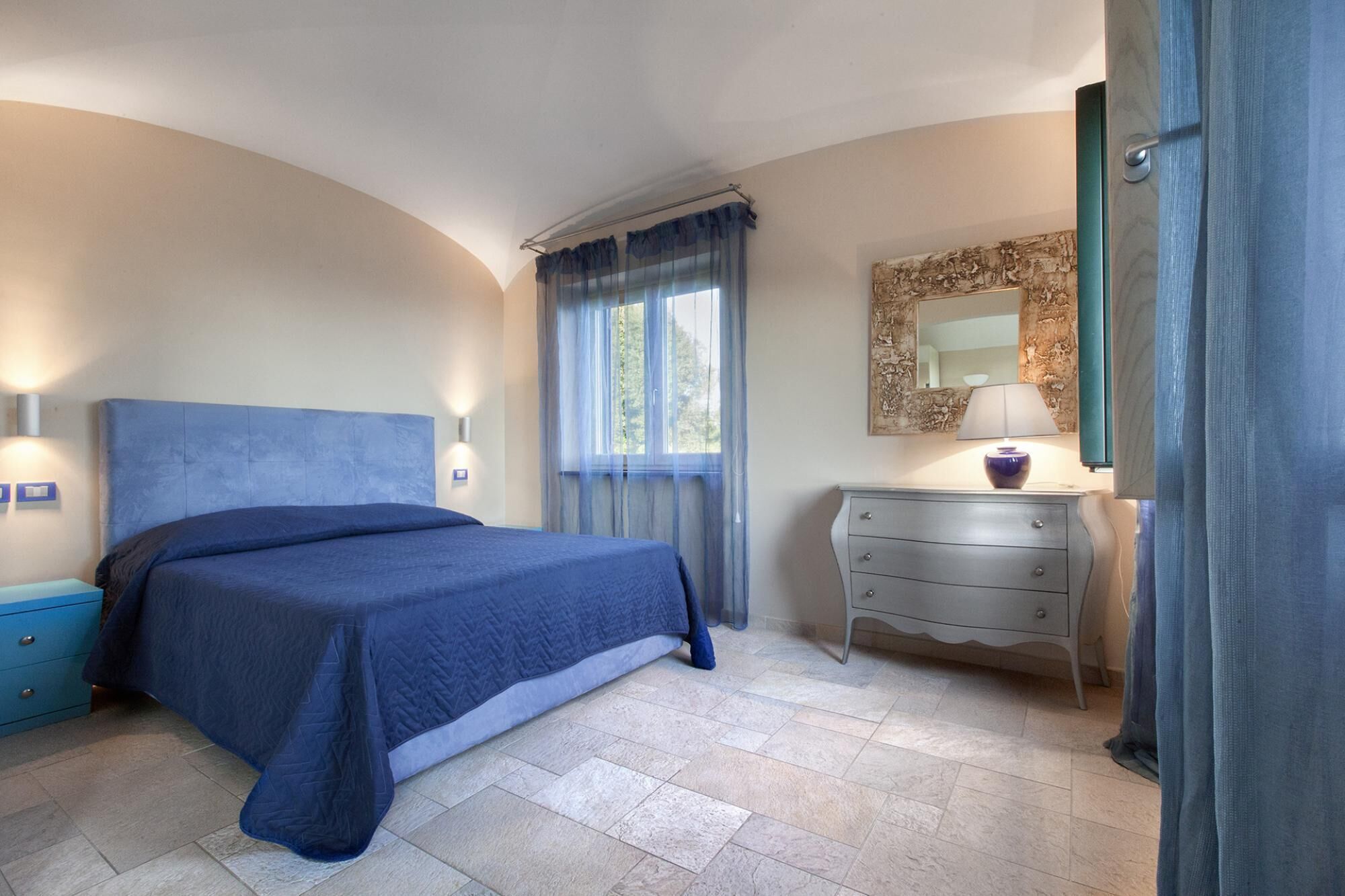 A bedroom with a bed, a dresser, a mirror, and a window with curtains.