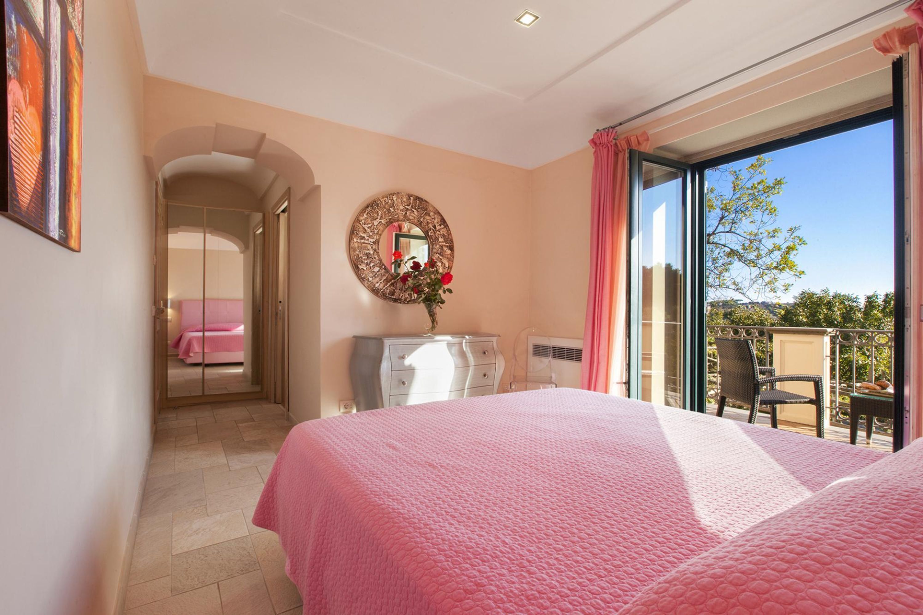 Ein Schlafzimmer mit einem großen Bett, einem Schminktisch, einem Spiegel und einer Glastür zum Balkon.