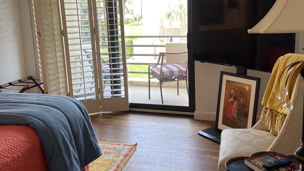A room with a bed, a chair, a table, a TV, and a balcony with a view of palm trees. - SAWGRASS OCEAN GATE PONTE VEDRA BEACH (Ponte Vedra Beach)