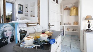 Une chambre d’hôtel avec un plateau de petit-déjeuner comprenant du café, des viennoiseries et une rose bleue. On y trouve également une bibliothèque avec des livres et un miroir.