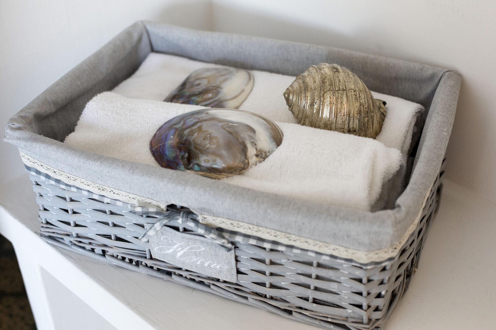 A wicker basket with a label, containing a seashell and two smooth stones.