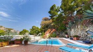 Una piscina en la azotea con sillas reclinables azules, rodeada de plantas en macetas y vistas a las montañas.