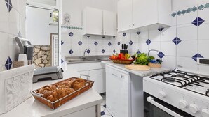 Una cocina con armarios blancos, estufa a gas, lavavajillas y una encimera con una cesta de croissants y un frutero.