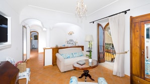 A spacious living room with a sofa, a round coffee table, and a chandelier. There is a wooden cabinet and a window with curtains. - Villa Zeus in Positano (Positano)