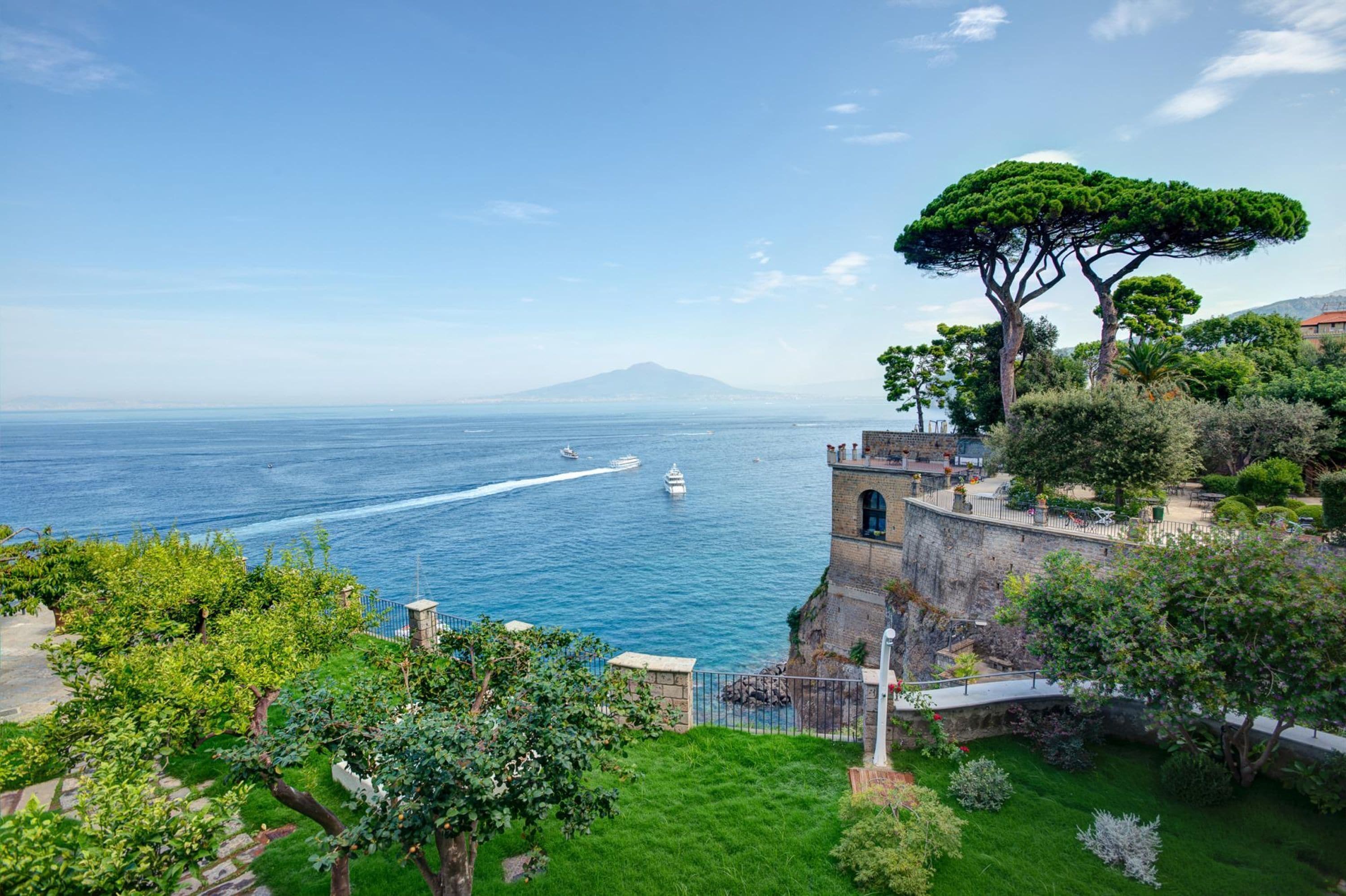 Vista costeira com uma torre histórica, vegetação exuberante e mar azul cristalino.