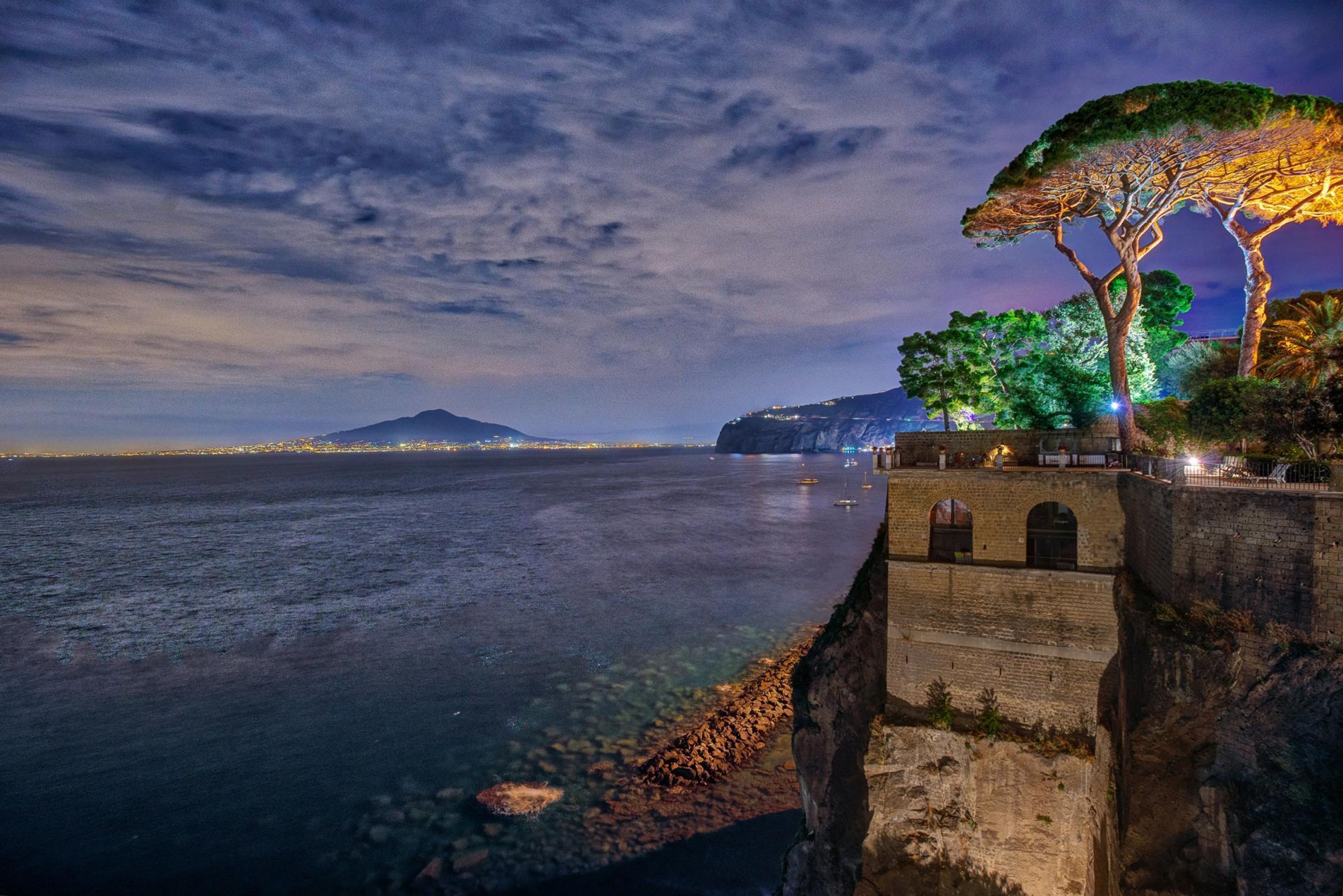 Escena costanera amb una paret de pedra i un arbre il·luminat per llums.