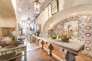 A kitchen with a marble countertop, hanging lights, and a tiled backsplash with a religious mural.