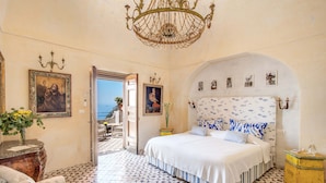 A bedroom with a bed, a chandelier, a painting, and a view through an open door. - Villa San Giacomo in Positano (Positano)