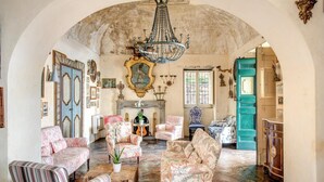 A spacious living room with a high arched ceiling, a chandelier, and a fireplace. There are several upholstered chairs and a striped armchair. - Villa San Giacomo 1 in Positano (Positano)