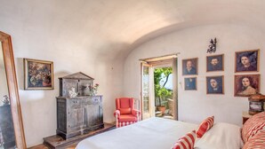 A bedroom with a large bed, a wooden cabinet, a red armchair, and several framed pictures on the wall. - Villa San Giacomo 1 in Positano (Positano)