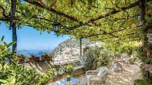 An outdoor patio with wicker furniture, potted plants, and a view of a coastal town. - Villa San Giacomo 1 in Positano (Positano)