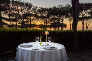 Een ronde tafel gedekt voor buiten eten, met uitzicht op bomen en een zonsondergang.