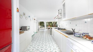 Una cocina con armarios blancos, un refrigerador rojo y piso de baldosas.
