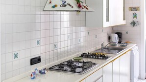 Una cocina con armarios blancos, una estufa a gas, un fregadero y azulejos decorativos en el salpicadero.