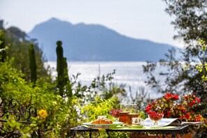 Une table avec un croissant, un verre de jus de fruits et un bol de fruits rouges, le tout disposé devant un paysage pittoresque composé d’une étendue d’eau et de montagnes.