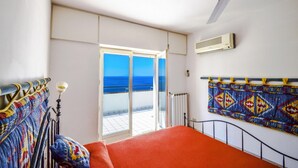 Een slaapkamer met een bed, een plafondventilator, uitzicht op zee en een kamerbreed gordijn.