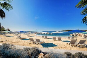 En strand med liggestole, parasoller og en klar, blå himmel.