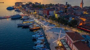 Una località costiera al crepuscolo con un porto turistico, edifici storici e una torre imponente.