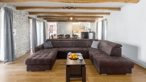 Un soggiorno con un ampio divano angolare, un tavolino in legno con della frutta e travi a vista al soffitto.