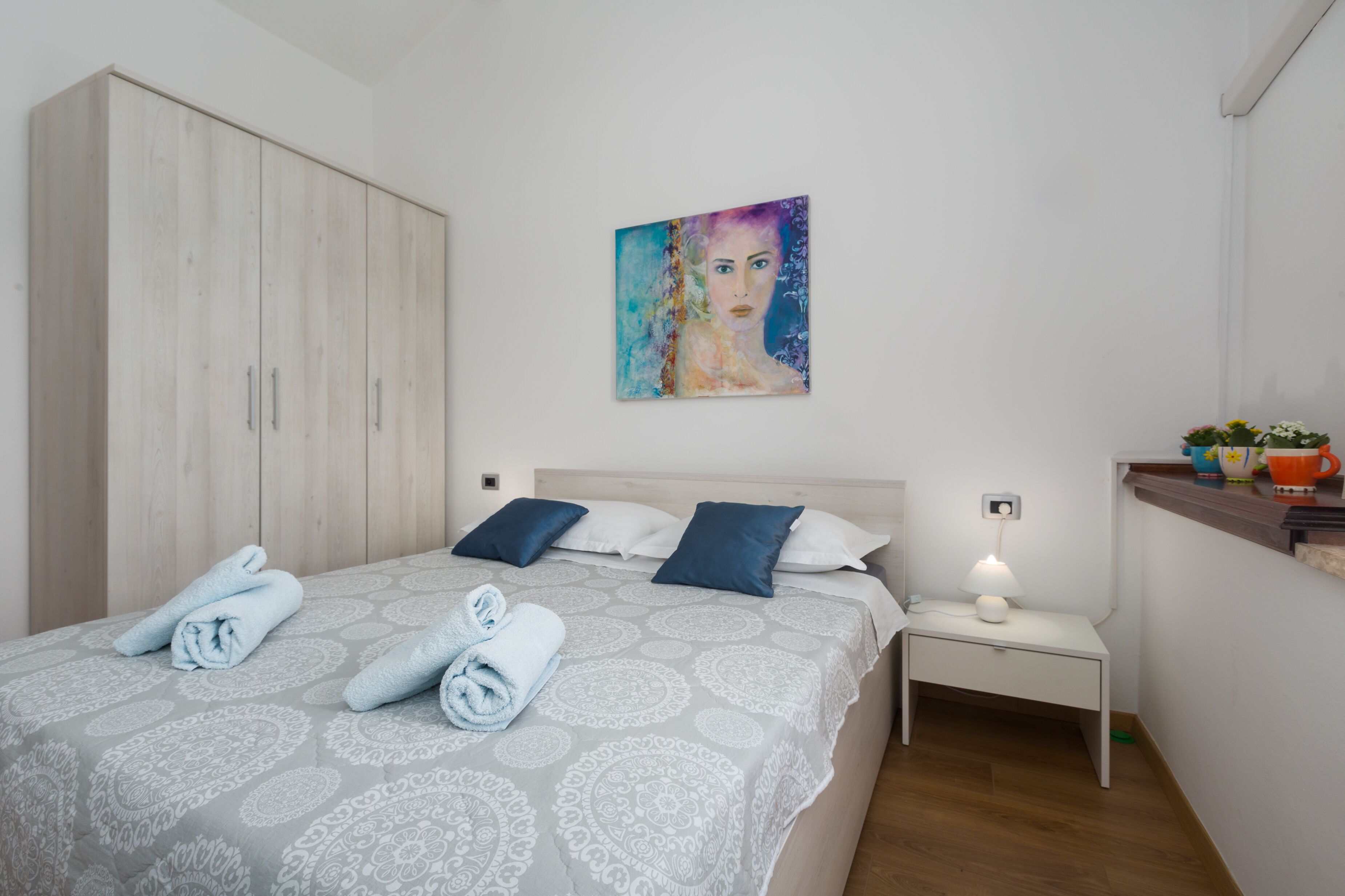 Une chambre à coucher avec un lit, des oreillers, une table de chevet, un tableau et une armoire.