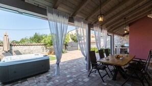 Un'area patio coperta con una vasca idromassaggio, un tavolo di legno con sedie e un muro in pietra sullo sfondo.