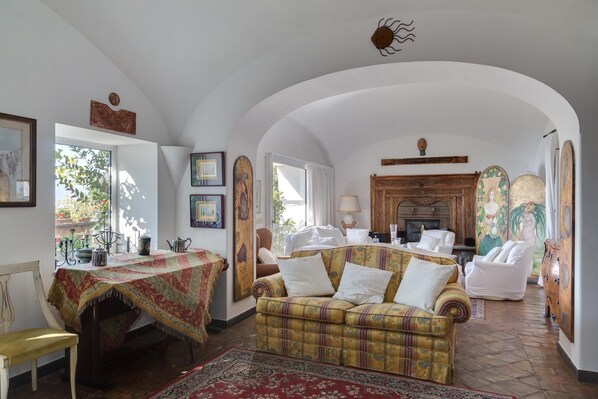 A spacious living room with a high arched ceiling, a fireplace, and a dining area with a table set for two. - Villa Era in Positano (Vico Equense)