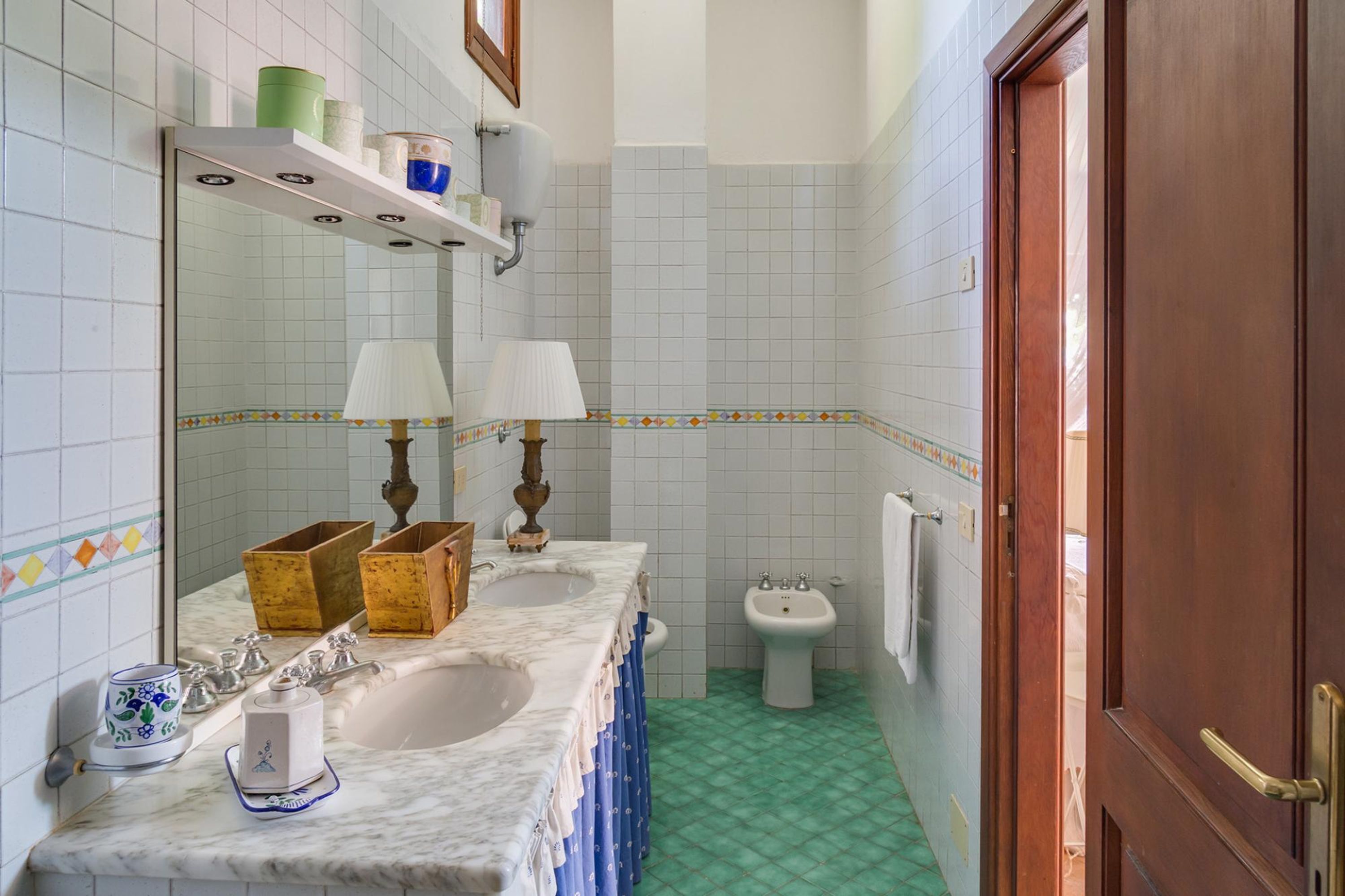 A bathroom with two sinks, a mirror, a vanity, a bidet, and a door.