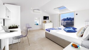 Un dormitorio moderno con cama, escritorio con computadora portátil, silla, cómoda y televisor.