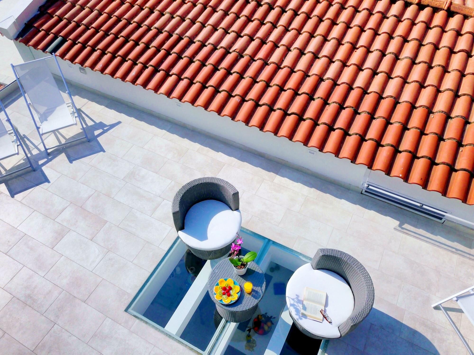 A rooftop terrace with a glass table, two wicker chairs, and a small potted plant.