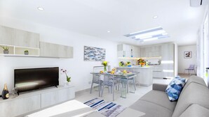 Una sala de estar moderna con una televisión de pantalla plana, un sofá y un comedor con una mesa de vidrio.