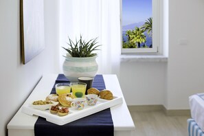 A breakfast tray with pastries, a plant, and a window view of palm trees and a mountain. - Appartamento Tramontano (Sorrento)