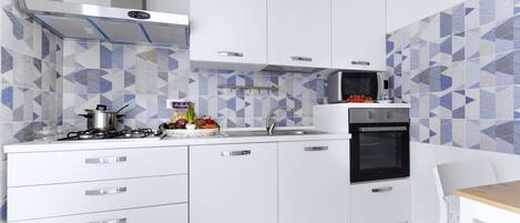 A modern kitchen with white cabinets, a gas stove, a microwave, and a sink.