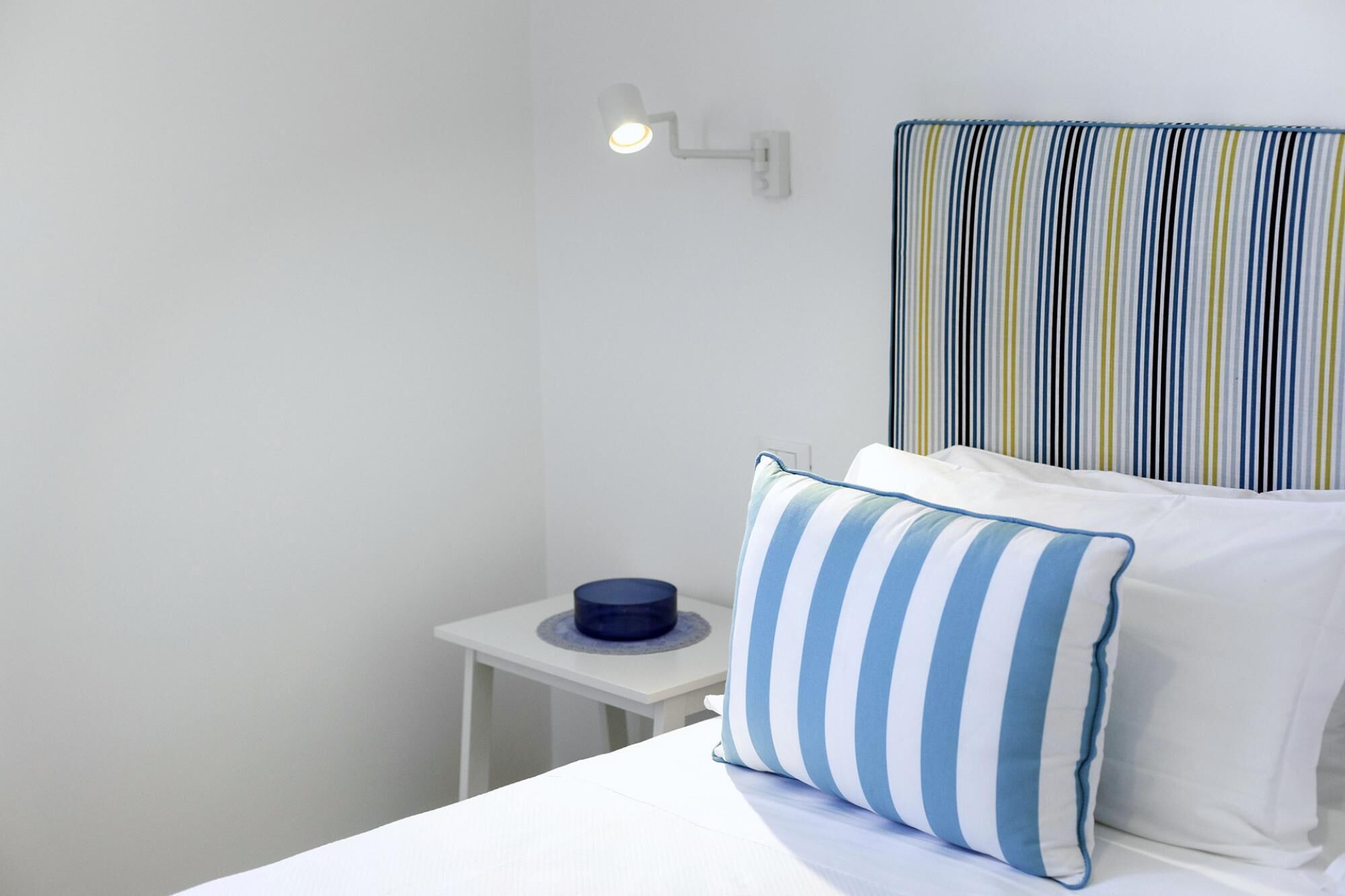 A hotel room with a bed, a bedside table, a lamp, and a striped headboard.