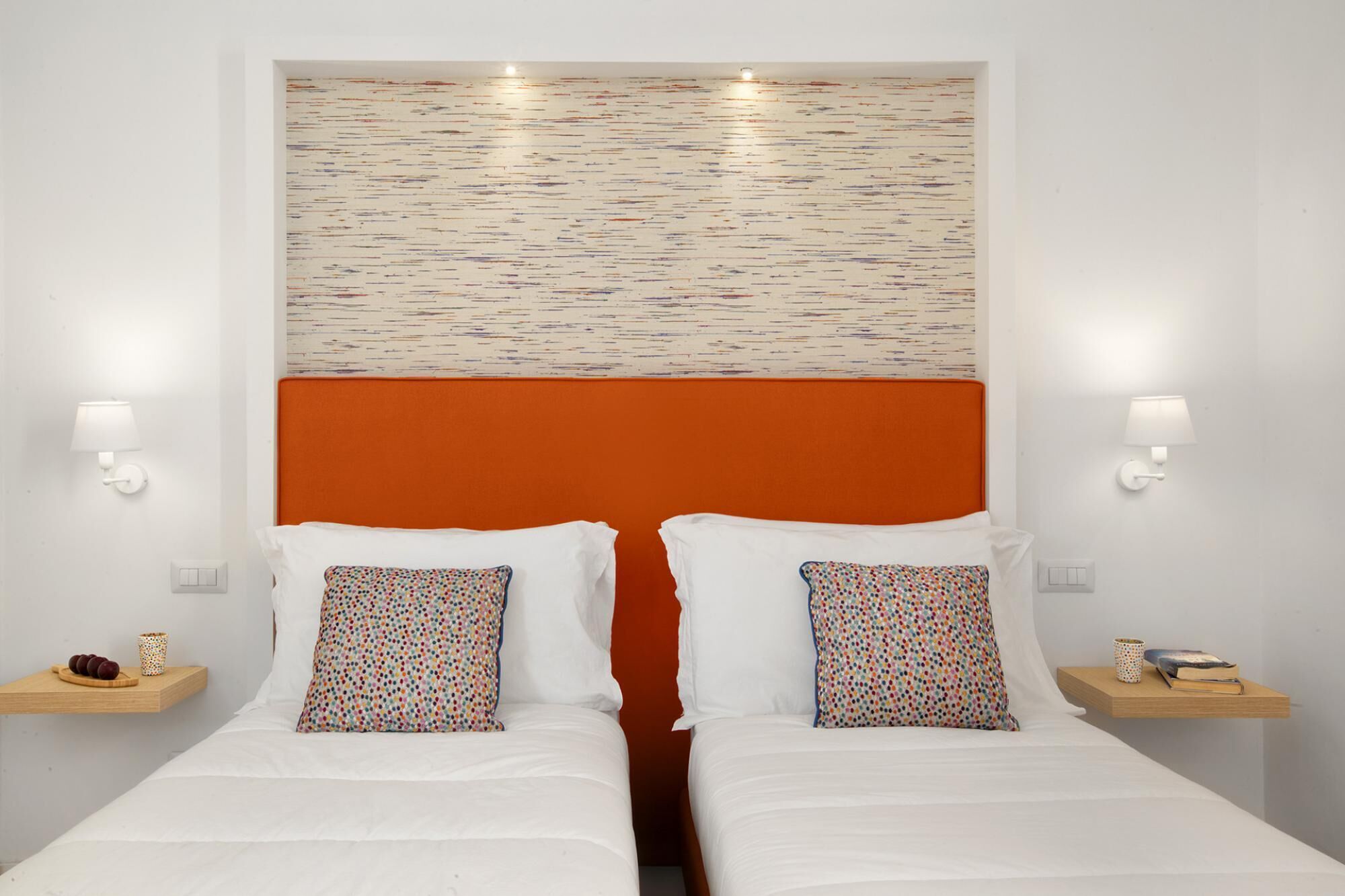 Ein Hotelzimmer mit zwei Betten, weißer Bettwäsche, einem orangefarbenen Kopfteil und einem farbenfrohen, abstrakten Wandbild.