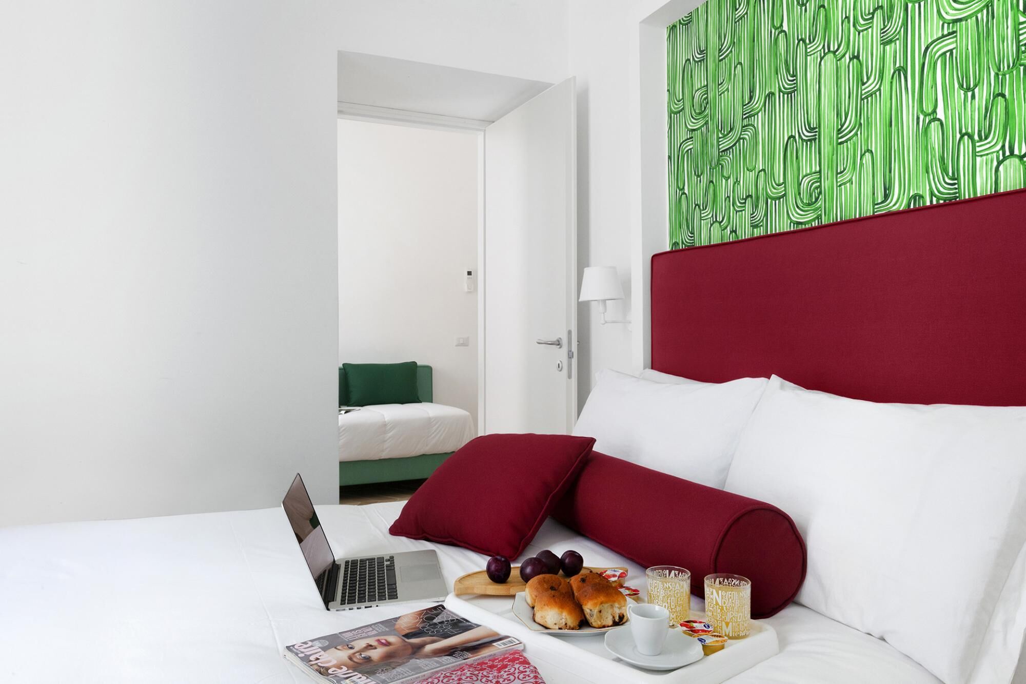 Une chambre d’hôtel avec un lit, un ordinateur portable, une assiette de pâtisseries et un magazine.