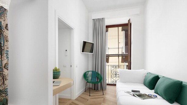 A modern, well-lit bedroom with a wooden floor, a white sofa with green cushions, a small desk with a laptop, a green chair, and a TV on the wall. - Casa 80 in Sorrento With 3 Bedrooms and 2 Bathrooms (Sorrento)