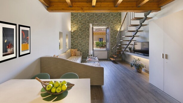 Ein modernes Interieur mit Holzboden, einem Essbereich mit Tisch und Stühlen, einer Couch und einer Treppe, die in eine obere Etage führt.