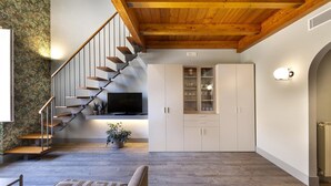 Ein modernes Interieur mit einer Holztreppe, einem Flachbildfernseher, weißen Schränken und einem gemusterten Teppich.