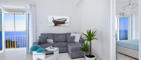 Ein modernes Wohnzimmer mit einem grauen Ecksofa, einem Glastisch, einer Topfpflanze und einem Bild von einem Boot.