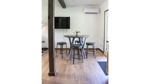 A room with a round table and four stools, a flat-screen TV mounted on the wall, and an air conditioning unit.