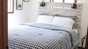 A bedroom with a checkered bedspread, a wooden headboard, and a small bedside table with a lamp.