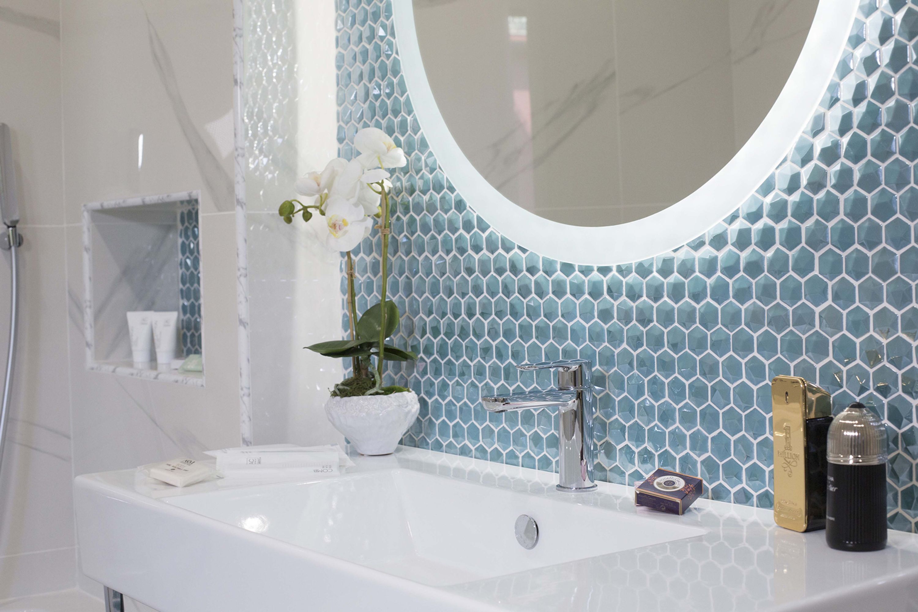 A bathroom with a white sink, a round mirror, and a blue hexagonal tile backsplash.