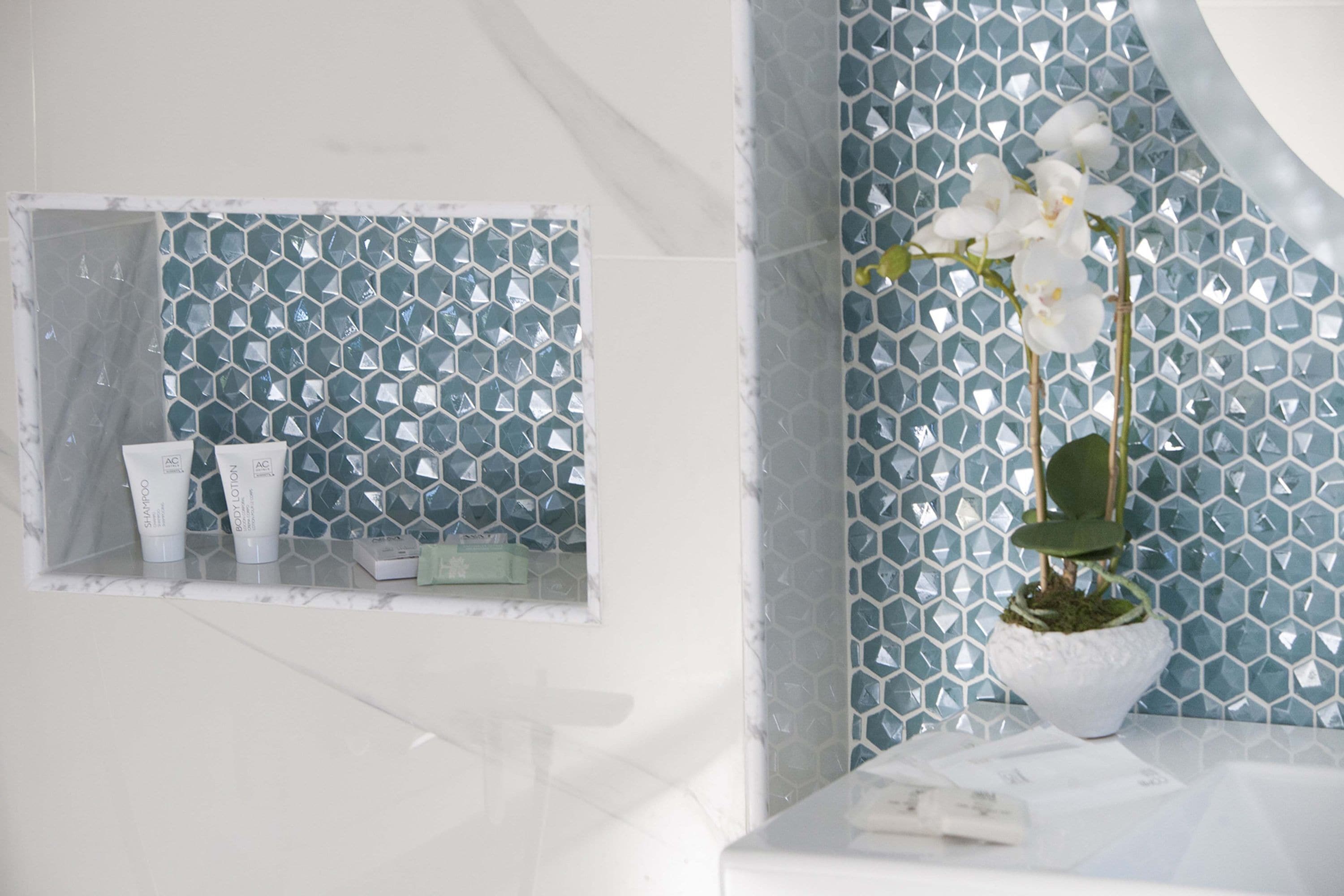 A bathroom with a mirror, a window with toiletries, and a potted orchid.